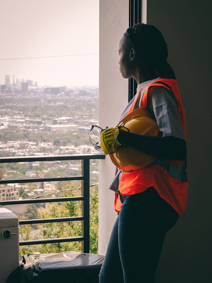 our-services-2 Female engineer in safety vest overlooking the city, holding helmet.