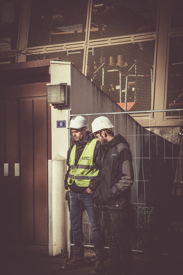 our-services-1 Two construction workers in safety gear standing outdoors at a building site, focused on work.